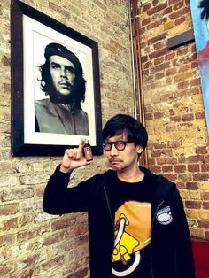 a man holding up a framed photo in front of a brick wall with a painting on it