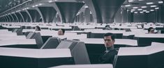 a man is sitting in an office cubicle with lots of desks and computers