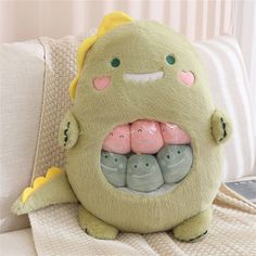 a green stuffed animal with three little pink ones in it's mouth on a couch