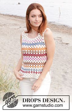 a woman standing on top of a sandy beach next to the ocean with her hands in her pockets