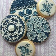 decorated cookies with blue and white frosting on a purple tablecloth next to lace