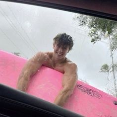 a man sitting on a pink surfboard in the back of a car, smiling