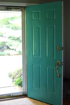 a bright green door is open in front of a window with a cat sitting on the floor