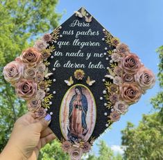 a hand holding up a graduation cap with roses on it and the image of mary magdalene