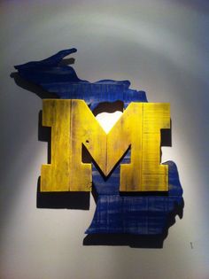 the letter m is made out of wood and painted blue, yellow and white colors