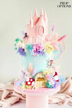 a pink cake with a castle on top and flowers around the base is decorated in pastel colors