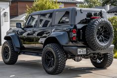 a black jeep is parked in front of a house with large tires on it's sides