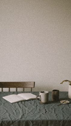 a table with a book, coffee cup and vase on it next to a bench