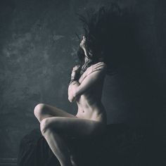 a naked woman sitting on the floor with her hair blowing in the wind over her head