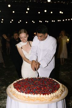 a man and woman cutting into a large cake on top of a white table cloth