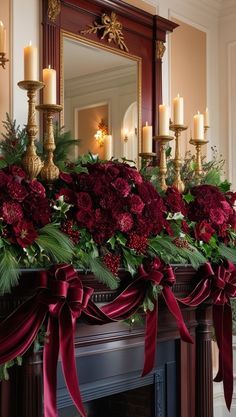 a mantel decorated with red flowers, greenery and candles in front of a mirror