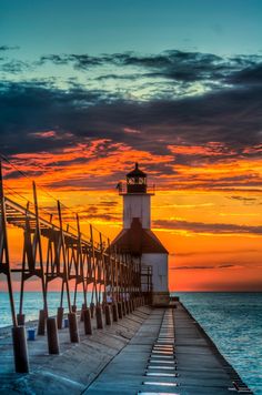 a light house sitting on the end of a pier next to the ocean at sunset