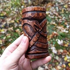 a hand holding a wooden carved cup in front of some leaves and trees on the ground