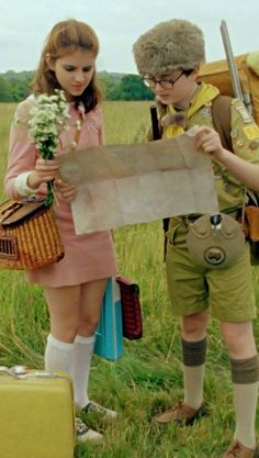 two children are standing in the grass looking at a map