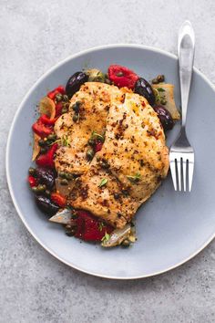 a white plate topped with chicken and vegetables next to a fork on top of a table