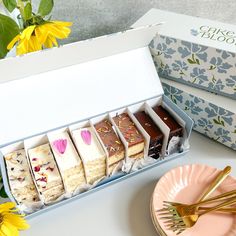 an assortment of desserts sitting in a box next to a plate with flowers on it