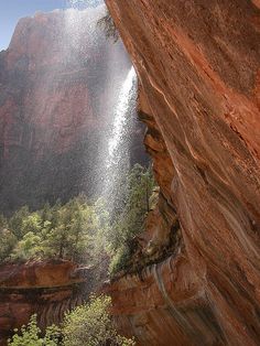 a man standing on the side of a cliff next to a waterfall with water coming out of it