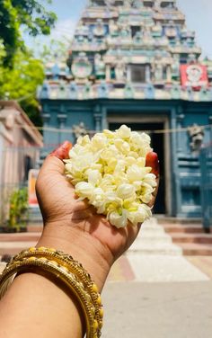 a hand holding a bunch of flowers in front of a blue and white temple building