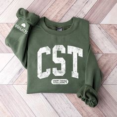 a green sweatshirt with the words cst printed on it sitting on a wooden floor