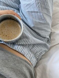 a person laying in bed holding a cup of coffee with both hands on their stomach