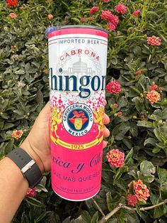 a person holding up a can of beer in front of some bushes and flowers with the caption's name on it