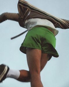 a man in green shorts and white shirt jumping up into the air with a backpack on his back