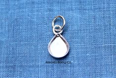 a silver charm with a tear hanging from it's end on a blue cloth