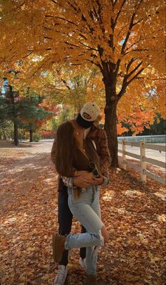 a man and woman kissing in front of a tree with autumn leaves on the ground