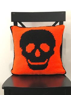 a crocheted skull pillow on top of a black chair with an orange cushion