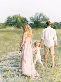 a man and woman are walking with their two children in a field, holding hands