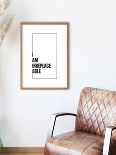 a brown leather chair sitting in front of a white wall with a framed poster on it