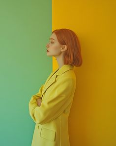 a woman with red hair standing in front of a yellow and green wall wearing a suit