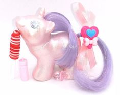 a pink pony with purple hair and a heart on it's tail next to lipstick