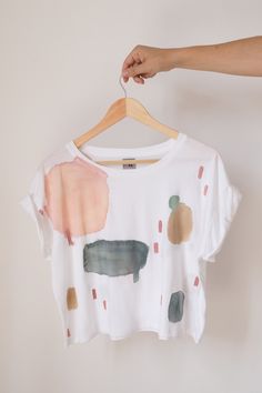 "Cropped organic cotton T-shirt, with round neck, white base and hand painted motifs in earth tones (dust pink, sand, gray green, gray, terracotta). This shirt is made in Africa with ethical craftsmanship. The cropped shape with rolled sleeves, combined with the manual water stains, make it perfect for both relaxed and sophisticated looks. You'll look radiant with a high-waisted jean or with dress pants and a jacket, achieving the \"effortless elegance\" effect that we love at APPA Studio. The \ White Hand Printed Crew Neck T-shirt, Hand Printed Organic Cotton T-shirt, Relaxed Fit, Hand Printed Organic Cotton T-shirt In Relaxed Fit, Hand Printed Relaxed Fit Organic Cotton T-shirt, Hand-printed Organic Cotton Crew Neck T-shirt, Hand Printed Organic Cotton Crew Neck T-shirt, Hand Printed Organic Cotton T-shirt, Organic Cotton Hand Printed Crew Neck T-shirt, Hand Printed Graphic Tee For Summer