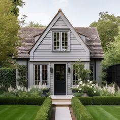 a gray house with white trim and trimmed hedges in the front yard is surrounded by lush greenery