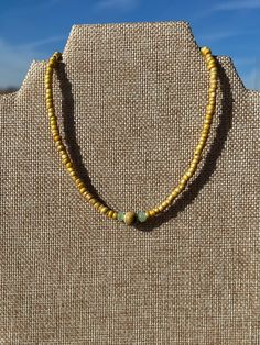 a yellow beaded necklace on a mannequin with a blue sky in the background