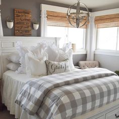 a white bed sitting in a bedroom next to two windows and a dresser with drawers