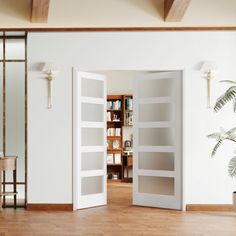 an open door leading to a living room with white walls and wooden floors, palm tree in the corner