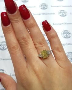 a woman's hand with red nail polish and a yellow diamond ring on it