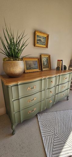 a green dresser with pictures and plants on top