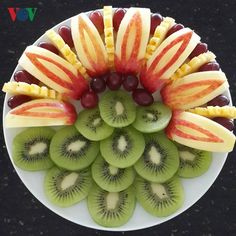 a white plate topped with sliced kiwis, grapes and apples on top of each other