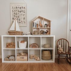 a white shelf filled with lots of toys on top of a hard wood floor next to a wooden rocking chair