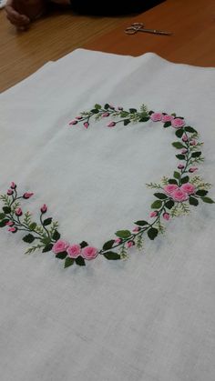 a white table cloth with pink flowers and green leaves in the shape of a heart