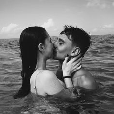 two people are kissing in the water while one person is holding his hand out to her face