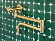 two brass faucets are attached to a green tiled wall