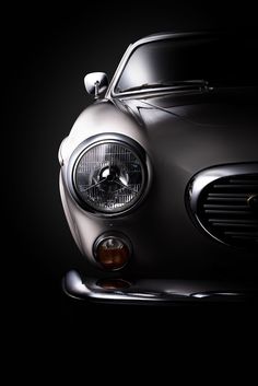 the front end of a silver sports car with its headlights turned on in dark lighting