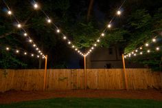 some lights that are on the side of a wooden fence in front of trees and grass