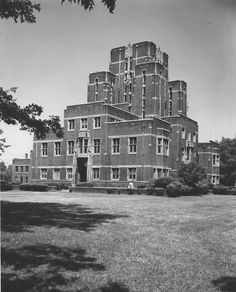 black and white photograph of an old brick building in the middle of a grassy area