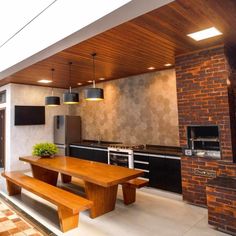 an outdoor kitchen and dining area with brick walls, wood ceilinging and large windows