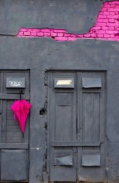 a pink umbrella is hanging on the side of a building with black doors and graffiti